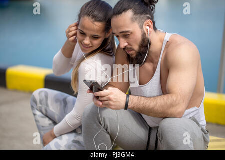Paar hören die Musik zusammen mit einem Ohrhörer sitzen auf Pier Stockfoto