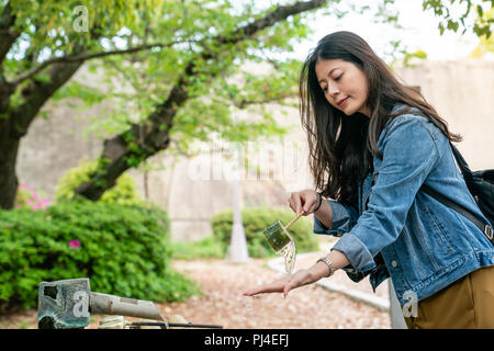 Hübsche asiatische Mädchen lächelnd und Bambus Schöpfkelle ihre Hand für ein reinigendes Ritual zu waschen. Stockfoto