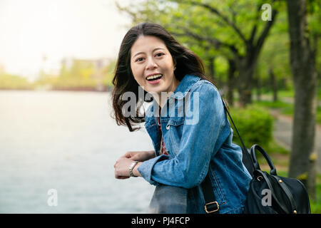 Schöne asiatische Frau lachend mit einem hübschen Lächeln und lehnte sich auf Leitplanke Neben freudig River. Stockfoto