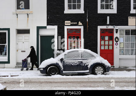 Wandern vorbei an den bunten Reihenhäuser im Winter Schnee in der Castle Street, Kirkcudbright, Dumfries und Galloway Stockfoto