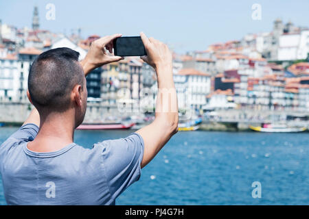 Nahaufnahme eines jungen kaukasischen Mann, von hinten gesehen, ein Bild von den Fluss Douro und Porto, Portugal, mit seinem Smartphone, von Vila Nova de Stockfoto