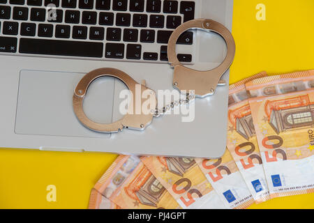 Geld unter Handschellen auf der Tastatur des Laptops. Hacker Kriminalität Konzept. Stockfoto