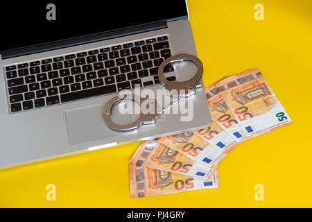 Geld unter Handschellen auf der Tastatur des Laptops. Hacker Kriminalität Konzept. Stockfoto