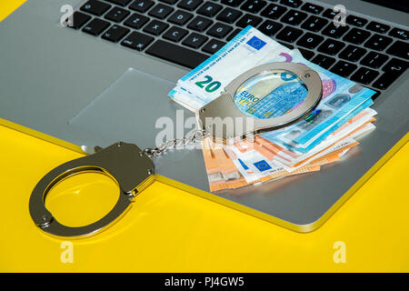 Geld unter Handschellen auf der Tastatur des Laptops. Hacker Kriminalität Konzept. Stockfoto