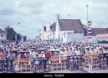 Rikscha Passagiere und Radfahrer am Bahnübergang in Jogjakarta, Indonesien, 1972 warten. Stockfoto