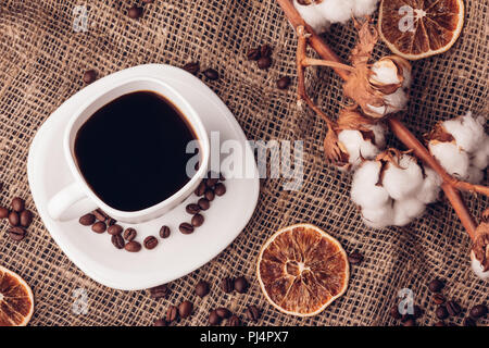 Weiße Tasse mit schwarzem Kaffee close-up auf der Leinwand neben einem Zweig der Baumwolle mit Knospen Stockfoto