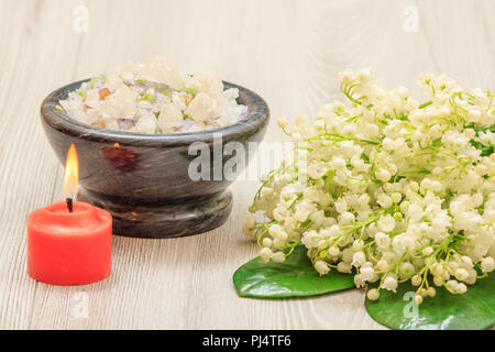 Brennende Kerze, Schale mit Salz und Blumenstrauß aus Lilien auf dem Tal auf Holz- Hintergrund. Wellness Produkte und Zubehör Stockfoto