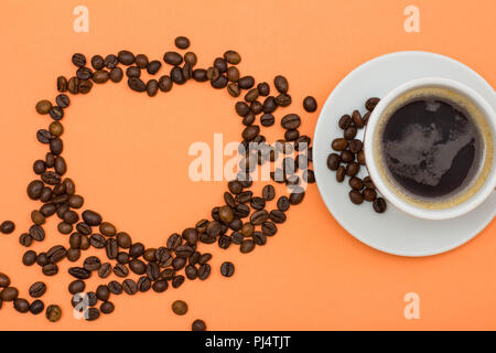 Weißes Porzellan Tasse Kaffee auf Untertasse mit Kaffeebohnen in der Form eines Herzens auf Pfirsich farbige Hintergründe gefaltet. Ansicht von oben Stockfoto