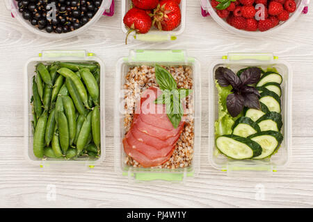 Kunststoff Mahlzeit prep Container grüne Erbsen, mit gekochten Buchweizen Brei und Scheiben von Fleisch, frischen Gurken und Salat, Johannisbeere, Erdbeere, Himbeere Stockfoto