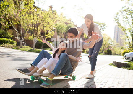Glückliche junge Familie spielen mit Skateboard Stockfoto
