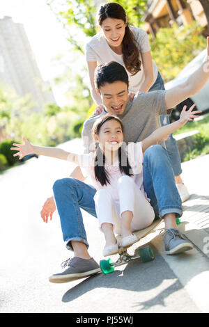 Glückliche junge Familie spielen mit Skateboard Stockfoto