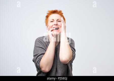 Reife Frau mit kurzen roten Haaren, die unter Stress leiden oder Kopfschmerzen Grimassen in den Schmerz, Hände auf Ihr Gesicht. Stockfoto