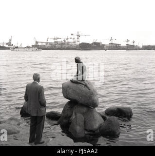 1950er Jahre, historische, Kopenhagen, Dänemark, am Wasser, am Ufer des Langeline, ein Herr bei "Die kleine Meerjungfrau", eine Bronzestatue auf einem Felsen von Edvard Eriksen suchen, Darstellung einer Meerjungfrau immer menschlich. Obwohl klein, ist es eines der berühmtesten Sehenswürdigkeiten der Stadt, und auf ein Zeichen aus einem Märchen der dänische Schriftsteller Hans Christian Andersen. Stockfoto