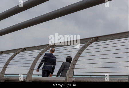 Ein Geschäftsmann und Geschäftsfrau zu Fuß über die Millennium Bridge über die Themse in London. Stockfoto