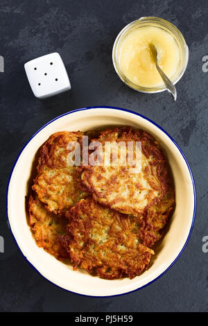 Frische, hausgemachte Reibekuchen oder Pfannkuchen in Emaille Schüssel mit Apfelmus auf der Seite, einem traditionellen deutschen Snack oder Gericht namens Kartoffelpuffer Stockfoto