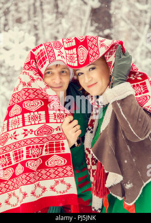 Junges Paar, Mann und Frau, Mann und Frau sind zu Fuß in Kostümen von Blumen, die typisch für die Elfen von Santa's Helfer in einem Winter Forest unter dem Schnee mit einer Truhe voller Geschenke und ein riesiges Candy Stockfoto