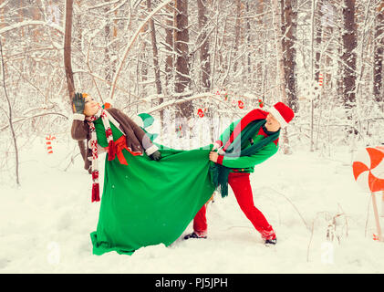 Junges Paar, Mann und Frau sind zu Fuß in Kostümen von Blumen, die typisch für die Elfen von Santa's Helfer in einem Winter Forest unter dem Schnee mit einem che Stockfoto
