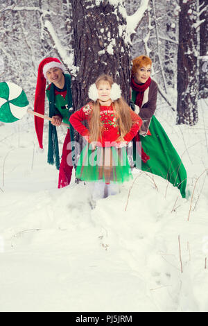 Familie in der traditionellen Weihnachtsstern Kostüme, Rot-Grün, Santa's Helfer - die Elfen, im Winter Wald mit einer Truhe von Geschenken und einem riesigen Candy Stockfoto