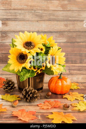 Herbst Stillleben mit Sonnenblumen Blumenstrauß in Holz- Übertopf, Kürbis, Blätter, Tannenzapfen, Eicheln auf rustikalen braunes Holz Hintergrund der Kontrollleiste. Stockfoto