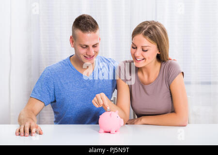 Junge glückliches Paar die Münze in Sparschwein. Stockfoto
