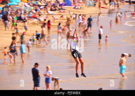 Eine Frau in einem Geschirr reist entlang einer Seilrutsche am Strand an, während Familien einen sonnigen Septembertag am Strand von Bournemouth, Großbritannien, genießen Stockfoto