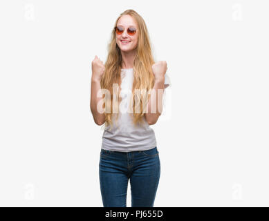 Blonde Teenager Frau mit Sonnenbrille schreien stolz und feiern Sieg und Erfolg sehr aufgeregt, jubelnde Emotion Stockfoto