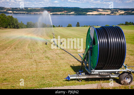 Reisen Sprinkler mit Schlauchhaspel Bewässerung Maschine spaying Wasser über einem Ackerland während einer Dürre im Sommer Stockfoto