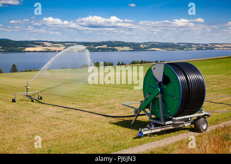 Reisen Sprinkler mit Schlauchhaspel Bewässerung Maschine spaying Wasser über einem Ackerland während einer Dürre im Sommer Stockfoto