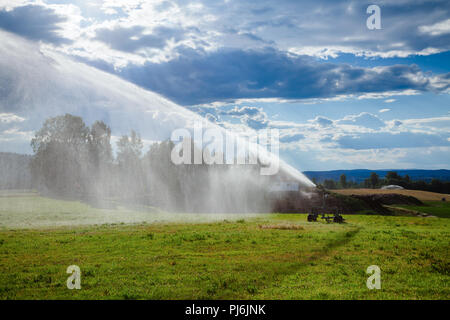 Tragbare Beregnung Maschine spaying Wasser über einem Ackerland während einer Dürre im Sommer Stockfoto