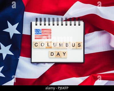 Notizblock mit leeren Seite, Holz- Buchstaben des Alphabets in der Form der Wörter Columbus Day auf dem Hintergrund der US-Flagge. Ansicht von oben, close-up Stockfoto