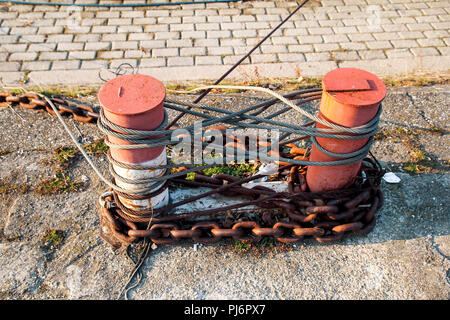 Braun Klampe für Schiffe, Boote. Alte Knecht: Dampf Kabinett mit einem gemeinsamen Grund auf die Docks von Metall rostig Braun Burgund, auf dem Gehäuse Metall schwere Kette Stockfoto