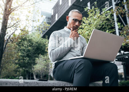 Unternehmer Arbeiten am Laptop sitzen im Freien mit Handy an seiner Seite. Unternehmer Managing Business sitzen Arbeiten im Freien. Stockfoto