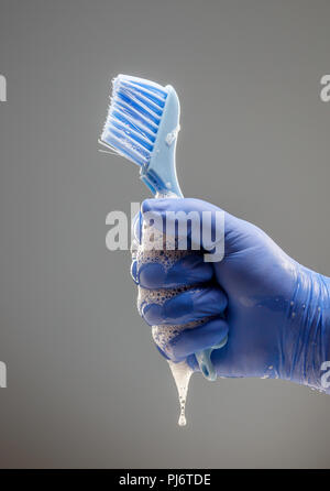 Die Hand eines Mannes in einem blauen Handschuh hält eine Bürste für die Reinigung mit einer tropfenden Schaum Stockfoto