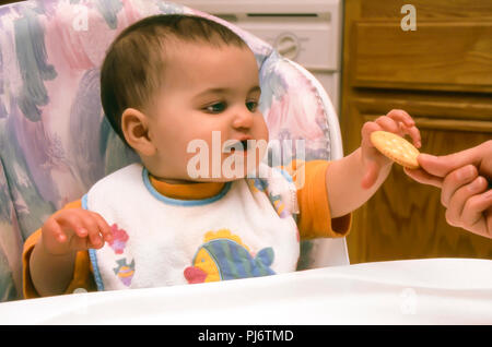 Baby Mädchen in kinderhochstuhl Hochstuhl sitzend erreichen für Cracker aus Mutters Hand. Herr © Myrleen Pearson... Ferguson Cate Stockfoto