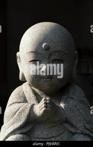 Cute Little Buddha Stein Statue beten und lächelnd mit geschlossenen Augen. Stockfoto