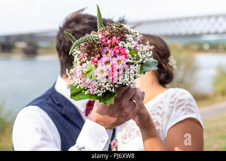 Seitenansicht der liebevollen Hochzeit paar hinter Strauß in Garten küssen. Stockfoto