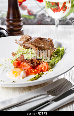 Klassische Caesar Salat mit Hähnchen, pochiertem Ei, Salatblätter, Cracker, Parmesan und Tomaten und Sahne Sause auf der Weiße, runde Platte hautnah. Restaurant Menü Stockfoto