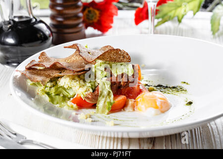 Klassische Caesar Salat mit Hähnchen, pochiertem Ei, Salatblätter, Cracker, Parmesan und Tomaten und Sahne Sause auf der Weiße, runde Platte hautnah. Restaurant Menü Stockfoto