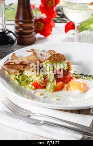 Klassische Caesar Salat mit Hähnchen, pochiertem Ei, Salatblätter, Cracker, Parmesan und Tomaten und Sahne Sause auf der Weiße, runde Platte hautnah. Restaurant Menü Stockfoto