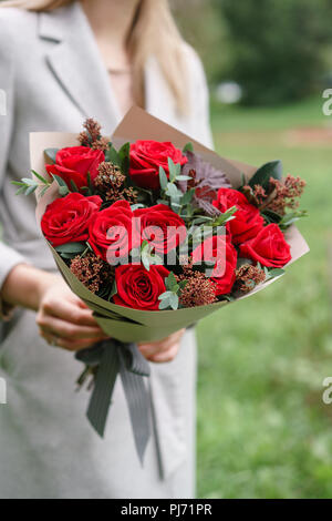 Schöne Frau mit einem schönen Herbst Bouquet. Blumenarrangement mit Nelken und Rote Garten Rosen. Farbe pink. grünen Rasen im Hintergrund Stockfoto