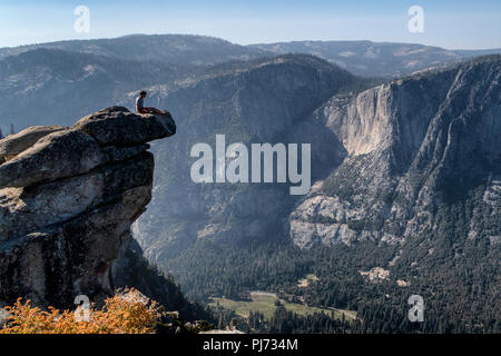 Ein sitzt auf einem überhängenden Felsen am Glacier Point genießen Sie den atemberaubenden Blick auf das Yosemite Valley, Kalifornien, USA. Stockfoto