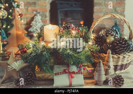 Gemütliche Weihnachten Zusammensetzung, Geschenke und Dekorationen auf dem Tisch vor dem Kamin mit Holzofen, beleuchtete Weihnachtsbaum mit Kugeln und oder Stockfoto