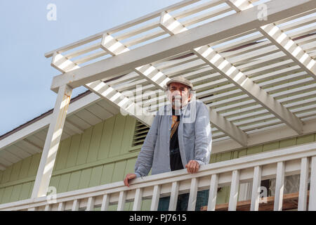 Senior, weißer Mann mit grauem Bart, mit Blick auf die Kamera, die oben stehend auf einem weißen Deck in der Sonne Licht Stockfoto