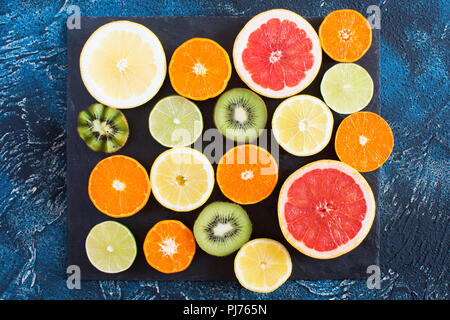 Früchte reich an Vitamin C: Orangen, Zitronen, Kiwis, Grapefruits und Zitronen auf der schwarzen Schiefer auf dem dunkelblauen Hintergrund, Ansicht von oben Stockfoto