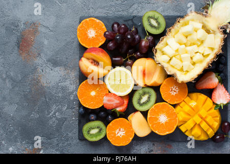 Rohe Früchte und Beeren platter Am grauen Stein, kopieren. Ananas, Mango, Satsuma, Kiwi, Pfirsiche, Orangen, Erdbeeren, Trauben, blau Stockfoto