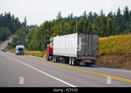 Red Old Fashion Big Rig cab - über Semi Truck Transport gefroren Cargo in voller Größe Kühlschrank Auflieger bergab gehen auf die Straße mit blühenden Stockfoto