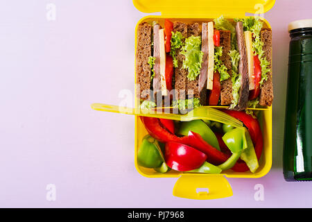 Gesunde Schule Lunch Box mit Rindfleisch Sandwich und frisches Gemüse, Flasche Wasser auf rosa Hintergrund. Ansicht von oben. Flach Stockfoto