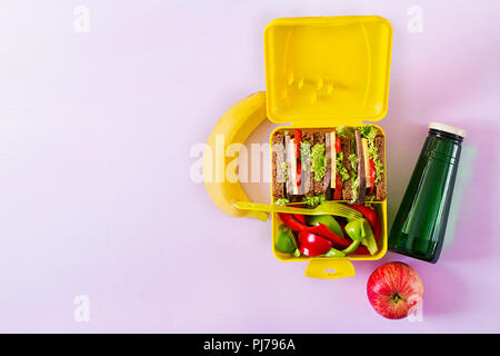 Gesunde Schule Lunch Box mit Rindfleisch Brötchen und frischem Gemüse, eine Flasche Wasser und Obst auf rosa Hintergrund. Ansicht von oben. Flach Stockfoto