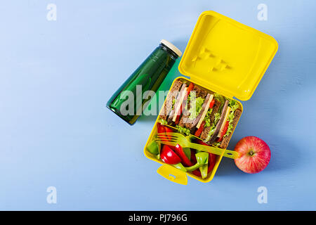 Gesunde Schule Lunch Box mit Rindfleisch Brötchen und frischem Gemüse, eine Flasche Wasser und Obst auf blauem Hintergrund. Ansicht von oben. Flach Stockfoto