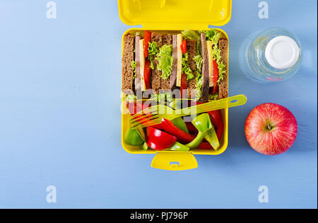 Gesunde Schule Lunch Box mit Rindfleisch Brötchen und frischem Gemüse, eine Flasche Wasser und Obst auf blauem Hintergrund. Ansicht von oben. Flach Stockfoto